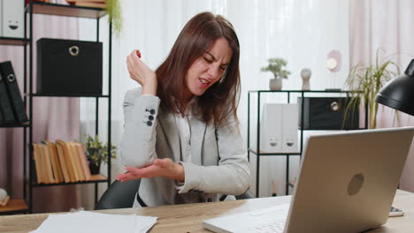 Mujer-De-Negocios-Sentada-En-La-Oficina-De-Su-Casa-Experimentando-Dolor-E-Incomodidad-En-La-Artritis-De-La-Mano-En-La-Articulación-Del-Codo