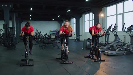 Un-Grupo-De-Chicas-Realiza-Una-Rutina-Cardiovascular-De-Entrenamiento-Aeróbico-En-Simuladores-De-Bicicletas,-Entrenamiento-En-Bicicleta.