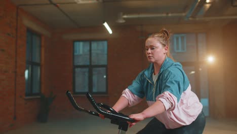 Healthy-Caucasian-woman-exercising-workout-on-stationary-cycling-machine-bike-in-gym,-slow-motion