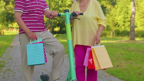 Elderly-stylish-couple-grandmother,-grandfather-after-shopping-with-bags-using-scooter-for-riding