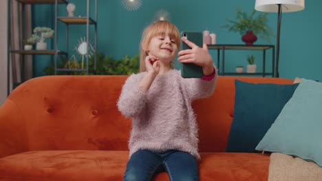 Niña-Pequeña-De-Escuela-Pequeña-Tomando-Una-Foto-Selfie-Con-Un-Teléfono-Inteligente-Mientras-Está-Sentada-En-Un-Sofá-En-Casa