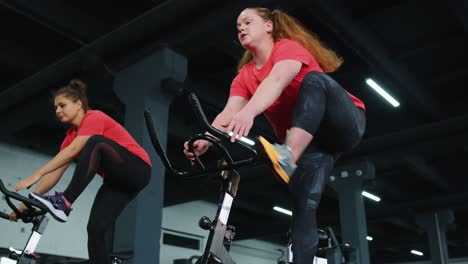 Group-athletic-girls-performing-aerobic-riding-training-exercises-on-cycling-stationary-bike-in-gym