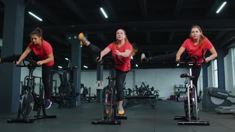 Grupo-Caucásico-Saludable-De-Mujeres-Haciendo-Ejercicio-En-Bicicleta-Estática-En-El-Gimnasio