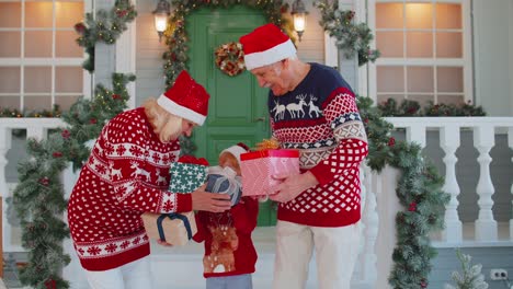 Abuelos-Mayores-Con-Nieta-Niña-Intercambiando-Regalos-Cerca-De-La-Casa-De-Navidad-Celebrando-La-Navidad