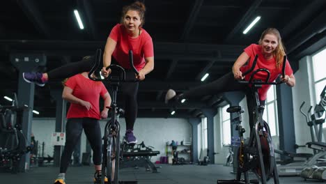 Group-athletic-girls-performing-aerobic-riding-training-exercises-on-cycling-stationary-bike-in-gym