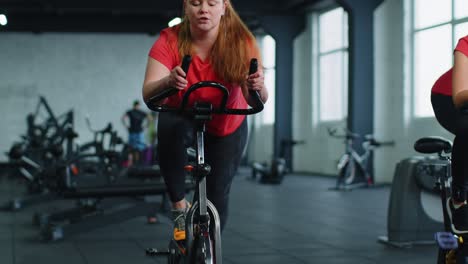 Group-of-smiling-friends-women-class-exercising,-training,-spinning-on-stationary-bike-at-modern-gym