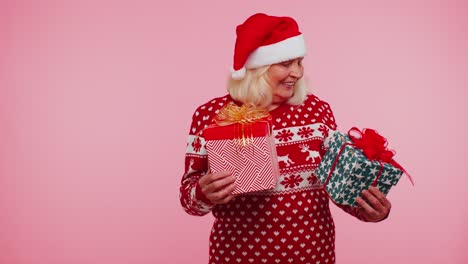 Abuela-Con-Suéter-De-Santa-Presentando-Una-Caja-De-Regalo-De-Navidad,-Extiende-Sus-Manos-A-La-Cámara