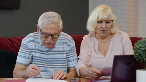 Stressed-senior-couple-discuss-unpaid-bank-debt-holding-bills,-doing-paperwork,-planning-budget