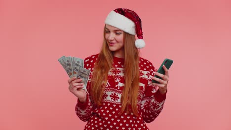 Mujer-En-Un-Suéter-Navideño-Mirando-Un-Teléfono-Inteligente-Regocijándose-Sinceramente-Por-Ganar-éxito-Suerte-Recibiendo-Dinero