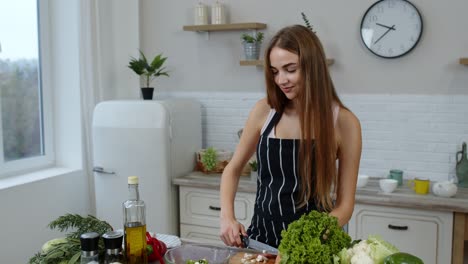 Vegan-girl-cooking-salad-with-raw-vegetables-while-looking-on-mobile-phone-for-online-recipe