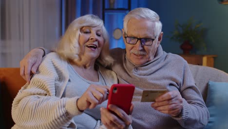 Abuela-Mayor-Con-Teléfono-Móvil-En-Casa-Haciendo-Compras-En-Línea-Con-Tarjeta-De-Crédito