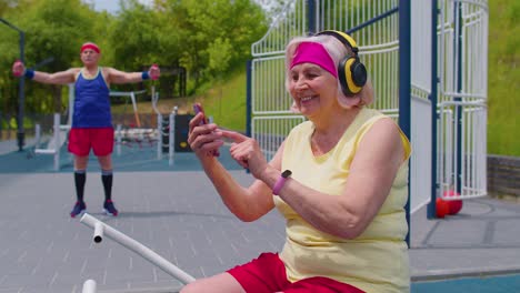 Mujer-Mayor-Después-Del-Entrenamiento-Deportivo-Escuchando-Música-Desde-Un-Teléfono-Móvil-Usando-Auriculares-En-El-Patio-De-Juegos