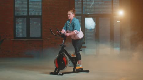 Chica-Atlética-Realizando-Ejercicios-De-Entrenamiento-Aeróbico-En-Bicicleta-Estática-En-Un-Gimnasio-Con-Niebla