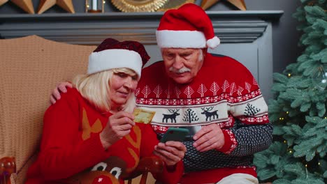 Abuela-De-La-Familia-Mayor-Usando-Tarjeta-Bancaria-De-Crédito-Y-Compras-De-Regalos-De-Navidad-Con-Teléfonos-Inteligentes