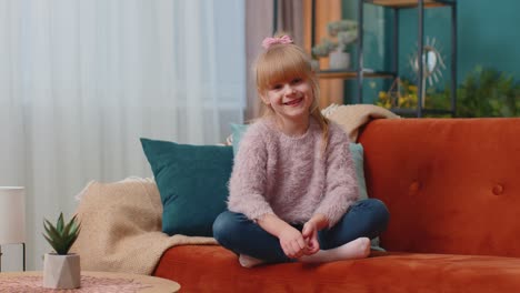 Retrato-De-Una-Niña-Adorable-Sentada-Sola-En-Un-Sofá-En-Casa-Mirando-La-Cámara-Y-Sonriendo