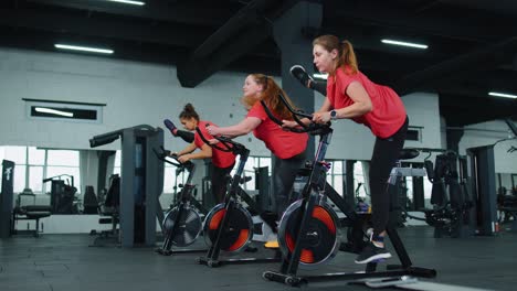 Group-of-girls-performs-aerobic-training-workout-cardio-routine-on-bike-simulators,-cycle-training