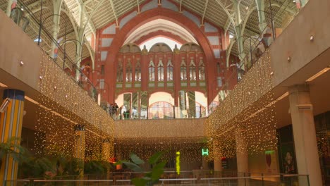 Decoración-Navideña-En-El-Interior-Del-Edificio-Del-Mercado-Con-Compradores-En-El-Mercado-De-Colón-En-Valencia,-España