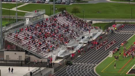 Parents-and-spectators-on-high-school-bleachers-watching-football-game-and-cheerleaders-in-USA