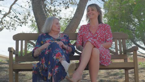 Charming-older-woman-sits-on-a-bench-chatting-with-a-young-woman,-she-smiles-and-enjoys-the-conversation