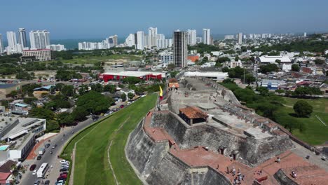 Aproximación-Aérea-A-Vista-De-Pájaro-Volando-Hacia-La-Bandera-Colombiana-Ondeando-Sobre-Una-Antigua-Fortaleza-Histórica-De-La-Ciudad-Colombiana-En-Cartagena,-Colombia