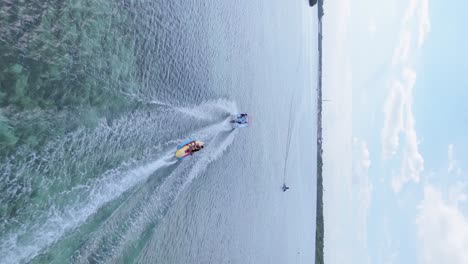 Vuelo-Vertical-De-Drones-Que-Muestra-Lancha-Rápida-Y-Niños-En-Un-Barco-Banana-En-El-Mar-Caribe