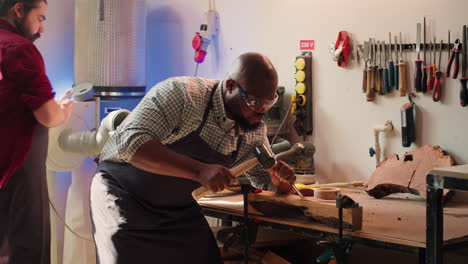 Artist-making-wood-sculptures-and-coworker-cleaning-workbench