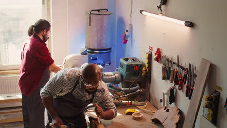 Artist-making-wood-sculptures-and-coworker-cleaning-workbench