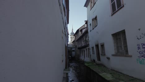 Urban-street-with-a-small-river-flowing-through-the-medieval-town-of-Colmar,-France