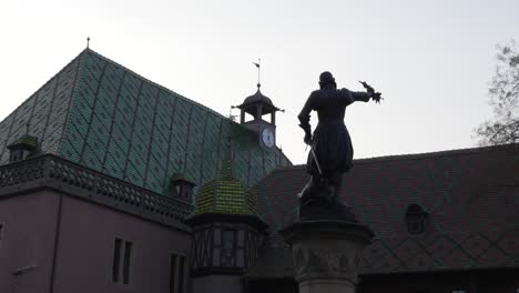 Vista-De-Cerca-Del-Monumento-A-La-Estatua-De-La-Fuente-Schwendi-Y-De-Un-Edificio-Medieval-Con-Entramado-De-Madera-En-La-Ciudad-Histórica