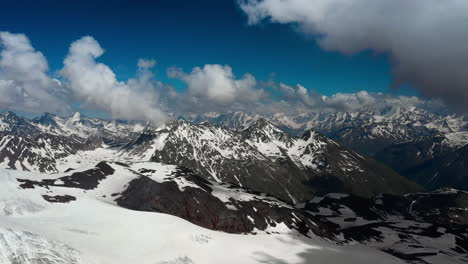 Air-flight-through-mountain-clouds-over-beautiful-snow-capped-peaks-of-mountains-and-glaciers.