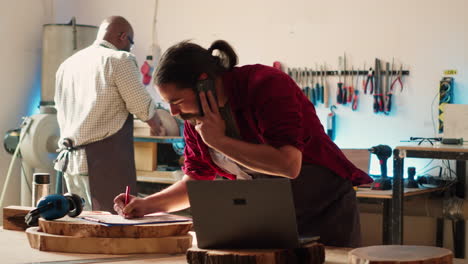 Carpenter-in-assembly-shop-having-friendly-conversation-on-cellphone-with-client