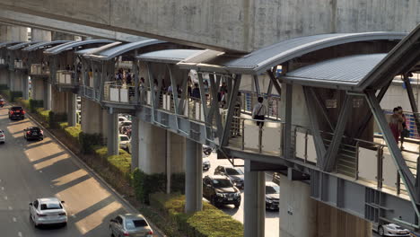 Pedestrians-walking-on-an-elevated-footbridge-over-a-busy-street-below,-in-a-busy-business-district-in-Bangkok,-Thailand