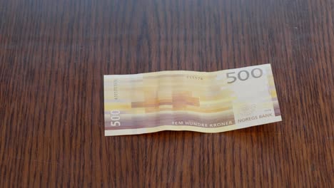 Hand-Placing-Norwegian-500-kr-Note-in-center-of-Wooden-Table