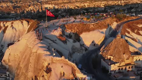 Volando-Sobre-Formaciones-Rocosas-Icónicas-De-Capadocia-Con-Turistas-Por-Todas-Partes-Y-Bandera-Roja-Turca