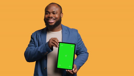 Amused-man-laughing-while-presenting-tablet-with-green-screen-display