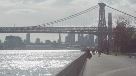 Heller-Nachmittagsblick-Entlang-Der-Uferpromenade-Des-East-River-Mit-Der-Williamsburg-Brücke-Im-Hintergrund