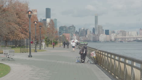 Herbstliche-Szene-Am-Ufer-Des-East-River-Mit-Menschen,-Die-In-New-York-Spazieren-Gehen,-Laufen-Und-Angeln