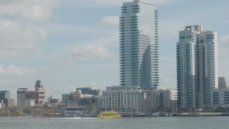 Yellow-Water-Taxi-Going-Across-East-River-With-Skyscrapers-In-Background-In-New-York