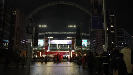 La-Gente-Hace-Cola-Con-Sus-Hijos-Para-Visitar-El-Camión-Navideño-De-Coca-Cola-Fuera-Del-Estadio-De-Wembley,-Debajo-Del-Famoso-Arco-Del-Estadio-Por-La-Noche.