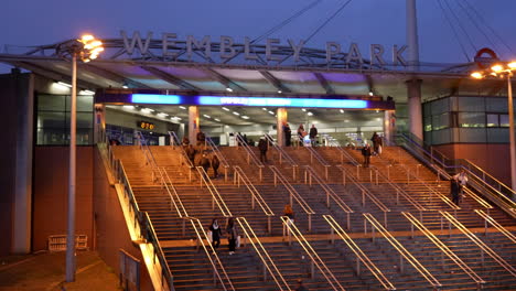 La-Gente-Sube-Y-Baja-Las-Escaleras-Que-Conducen-A-La-Entrada-Principal-De-La-Estación-De-Tren-Subterráneo-De-Wembley-Park-Al-Atardecer