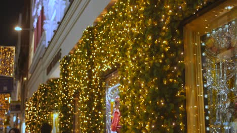 Tilt-down-shot-of-Christmas-deco-on-the-outer-facade-of-a-shop-in-Dublin,-Ireland-with-locals-passing-by-at-night-time