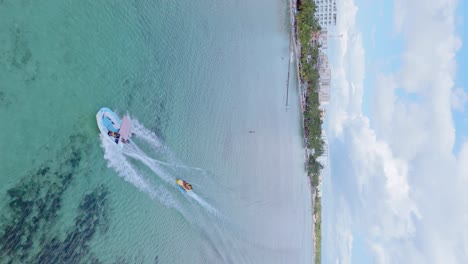 Disparo-Vertical-De-Un-Turista-En-Un-Barco-Banana-Tirando-De-Una-Lancha-Motora-En-El-Mar-Caribe