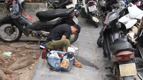 Shoe-cleaner-sitting-on-pavement-brushing-and-rubbing-customer-footwear