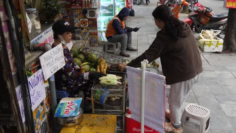 Street-vendor-seated-at-stall-grilling-and-preparing-corn-for-sale