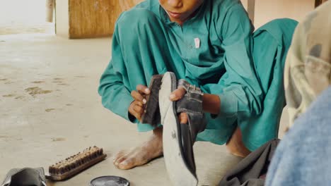 Close-up-shot-of-young-boy-polishing-leather-slippers-while-on-floor-In-Sindh,-Pakistan-at-daytime