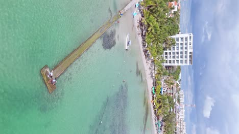 Vertikale-Drohnenaufnahme-Eines-Touristen,-Der-Im-Sommer-Auf-Dem-Steg-An-Der-Playa-Boca-Chica-Am-Sandstrand-Mit-Palmen-Spaziert---Santo-Domingo,-Dominikanische-Republik