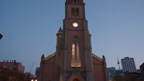 Catedral-De-Myeongdong-Al-Atardecer-Con-Gente-Abarrotada-Caminando-En-La-Ciudad-De-Seúl---Inclinación-En-Tiempo-Real-Hacia-Abajo