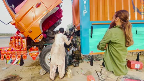 Zoom-in-shot-of-a-mechanic-repairing-the-engine-of-a-container-truck-by-the-side-of-a-road-after-it-broke-down-on-a-highway-at-daytime