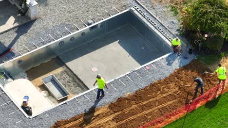 Trabajadores-Construyendo-Una-Piscina,-Colocando-Grava-Y-Cimientos,-Con-Equipo-De-Seguridad