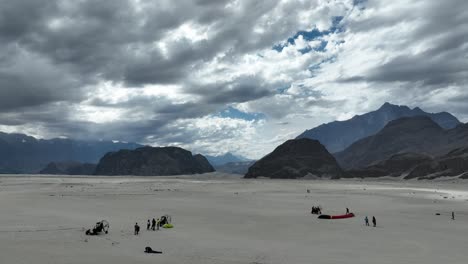 Drones-Aéreos-Avanzando-Sobre-Parapentes-Preparándose-Para-Volar-A-Lo-Largo-Del-Desierto-De-Sarfaranga,-Rodeado-De-Montañas-En-Skardu,-Pakistán-En-Un-Día-Nublado